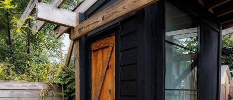 Una pequeña estructura de madera con puerta de cristal, un banco afuera y una valla de madera al fondo.