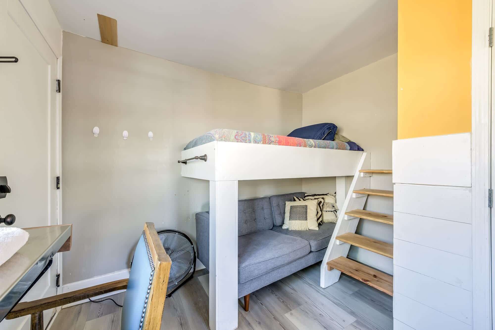 A compact room with a bunk bed, a sofa, a small table, and a ladder.