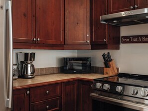 A kitchen with wooden cabinets, a microwave, a coffee maker, and a stove. - MiniPutt ~ Arcade ~ Pool ~ Playground ~ Golf & Ski (Mont-Tremblant)