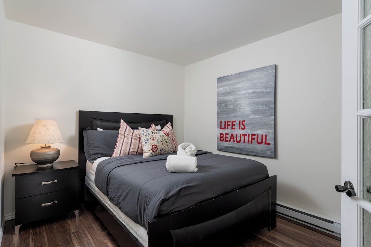 A bedroom with a bed, nightstand, lamp, and a motivational quote on the wall.
