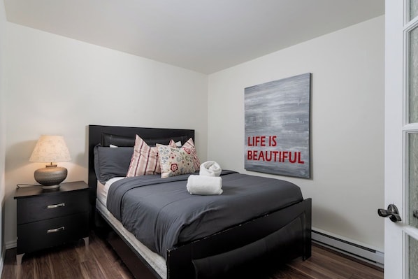 Un dormitorio con cama, mesita de noche, lámpara y una frase motivacional en la pared.