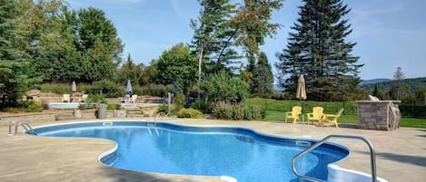 A swimming pool with a curved edge, surrounded by a concrete deck. There are lounge chairs and a small stone structure in the background.