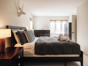 A bedroom with a bed, bedside table, dresser, and a window with curtains.