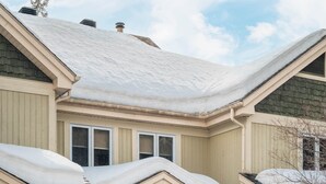 Una casa de dos pisos con techo nevado y porche delantero.