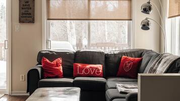 Ein Wohnzimmer mit einem Ecksofa, roten Kissen, einem Couchtisch und einer Wandlampe.