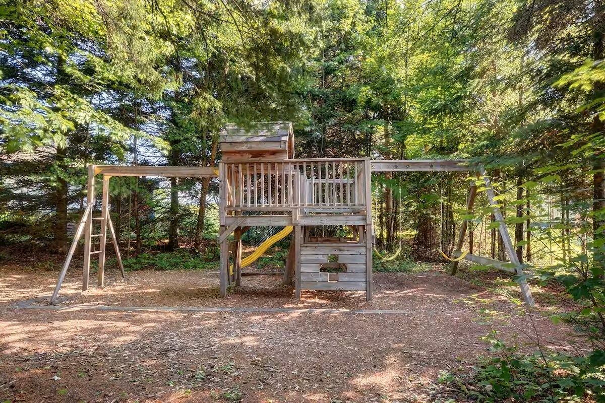 A wooden play structure in a forested area with a ladder and a slide.