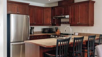 Una cocina moderna con armarios de madera, un refrigerador de acero inoxidable, una isla central con taburetes de bar y un horno empotrado.