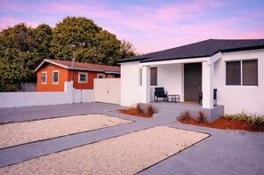 Ein modernes, zweistöckiges Haus mit Terrasse, weißem Zaun und Baum im Hintergrund.