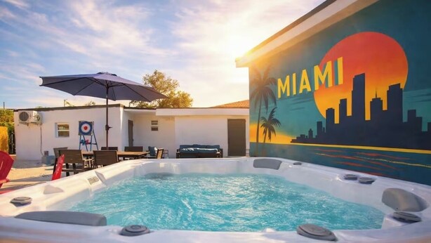 Zona de piscina con un mural al atardecer, sillas de descanso y un área de estar cubierta.