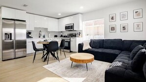 Una cocina moderna con armarios blancos, un sofá negro y una mesa de centro redonda de madera.