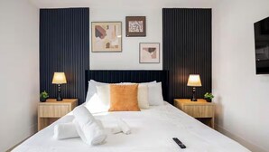 Habitación de hotel con una cama grande, dos mesitas de noche con lámparas, un televisor en la pared y cuadros.