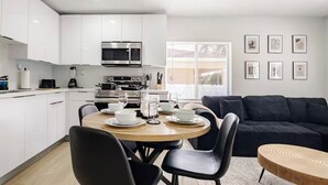 Una cocina moderna con armarios blancos, un microondas y un comedor con una mesa redonda y sillas negras.