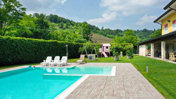 Ein Swimmingpool mit Liegestühlen, einem Spielbereich für Kinder und einem Haus im Hintergrund.