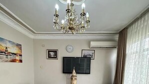 Un salon comprenant un canapé, des fauteuils, une table basse, un lustre, un téléviseur et un tapis à motifs.