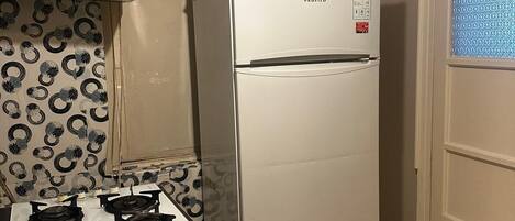 A compact kitchen with a white refrigerator, a gas stove, and patterned wallpaper.