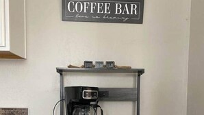 Cantinho de café com máquina de café, prateleira com rótulos de café, creme e açúcar, e uma caixa de café Brewed Light.