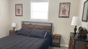 Quarto com cama grande, duas mesas de cabeceira, cômoda e duas pinturas penduradas na parede.