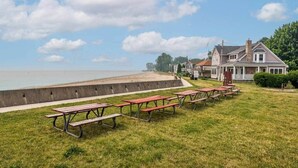 A grassy area with picnic tables and a beach in the background. - Beach Goer’s Paradise (Luna Pier)