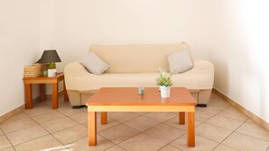 Ein Wohnzimmer mit einem beigefarbenen Sofa, einem Holztisch, einem kleinen Beistelltisch mit Lampe und einer Topfpflanze.
