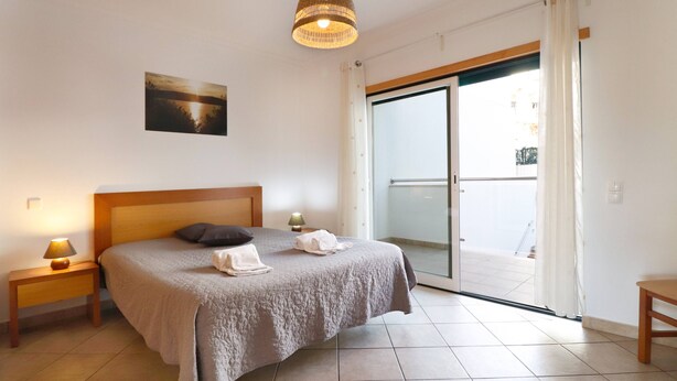 Ein Schlafzimmer mit Bett, Nachttisch, Lampe, einem Gemälde und einer Glastür zu einem Balkon.
