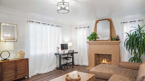 Un salon avec une cheminée, un canapé, une table basse en bois, un bureau avec un ordinateur et un miroir au-dessus de la cheminée.