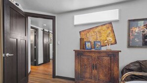 A hallway with wooden flooring, a dark wooden door, a white wall, a wooden cabinet with books, a map, and a framed picture.