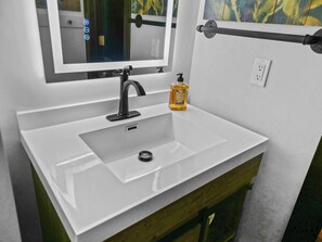 A white bathroom sink with a black faucet, a mirror above it, and a bottle of hand soap on the counter.