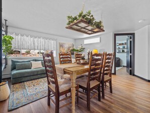 A dining area with a wooden table and chairs, a hanging plant, and a view of a garden through a window.