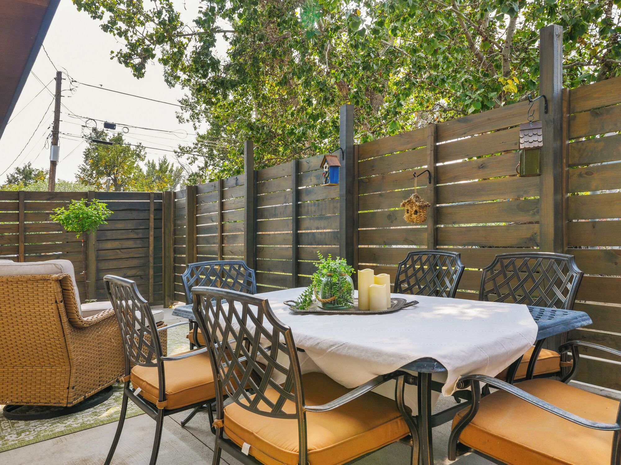 Une terrasse extérieure avec une table dressée pour quatre personnes, entourée de chaises en osier dotées de coussins.
