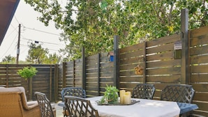 An outdoor patio with a table set for four, surrounded by wicker chairs with cushions.