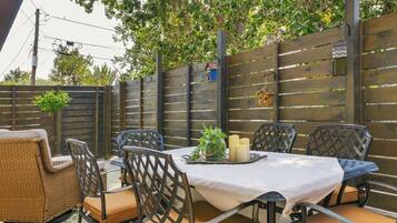 Une terrasse extérieure avec une table dressée pour quatre personnes, entourée de chaises en osier dotées de coussins.