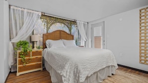 A bedroom with a wooden headboard, white bedding, a wicker nightstand with a lamp, and a woven rug.