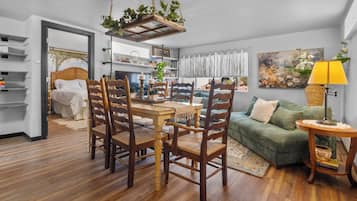 Un salon chaleureux avec un coin repas, un canapé vert, un plancher en bois et une plante suspendue.