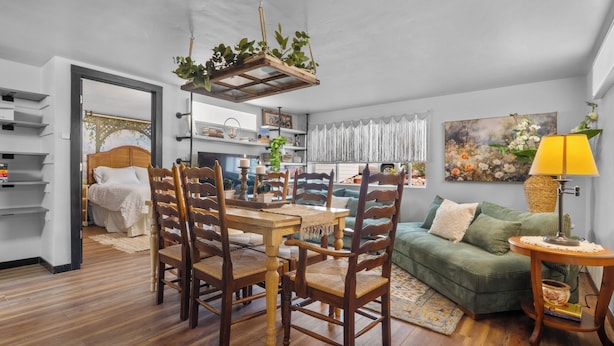 A cozy living room with a dining area, a green sofa, wooden flooring, and a hanging plant.