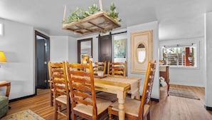 A dining area with a wooden table and chairs, a hanging plant, and a framed picture on the wall.