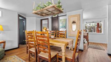Un coin repas avec une table et des chaises en bois, une plante suspendue et un tableau encadré au mur.