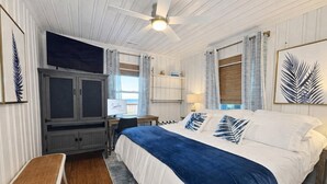 A bedroom with a bed, a desk, a chair, a ceiling fan, and a window with blinds.