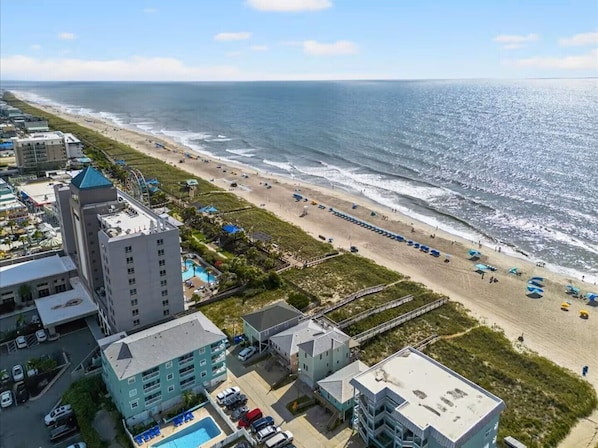 A coastal hotel with multiple buildings, a beach, and a pier.