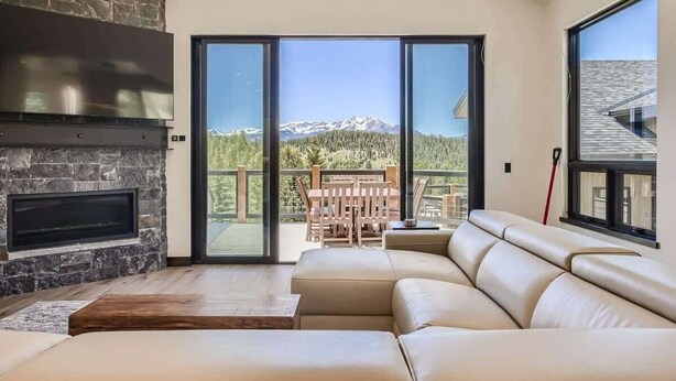 Un soggiorno moderno con camino in pietra, un divano ampio e una porta vetrata scorrevole che dà su un balcone con vista sulle montagne.