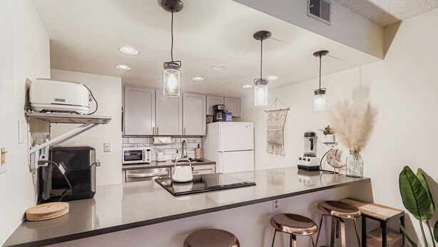 A modern kitchen with a central island, bar stools, a coffee machine, and pendant lighting. - Frisco Hotspot-Hot tub&More, Sleeps 4 (Frisco)