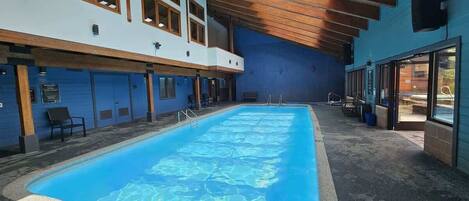 Een binnenzwembad met een helderblauw wateroppervlak, houten balken in het plafond en een blauwe muur.