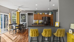 A modern kitchen with wooden cabinets, a black refrigerator, and a yellow bar stool. - The Yellow House - hot tub, pool table, fire pit, 6 bedrooms (Liberty)