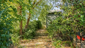A stone staircase surrounded by lush greenery and trees, leading to a building with a sloped roof. - The Yellow House - hot tub, pool table, fire pit, 6 bedrooms (Liberty)