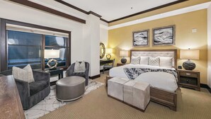 Ein Hotelzimmer mit einem großen Bett, zwei Nachttischen, einem Sofa, einem runden Hocker und einem Schreibtisch mit Stuhl.
