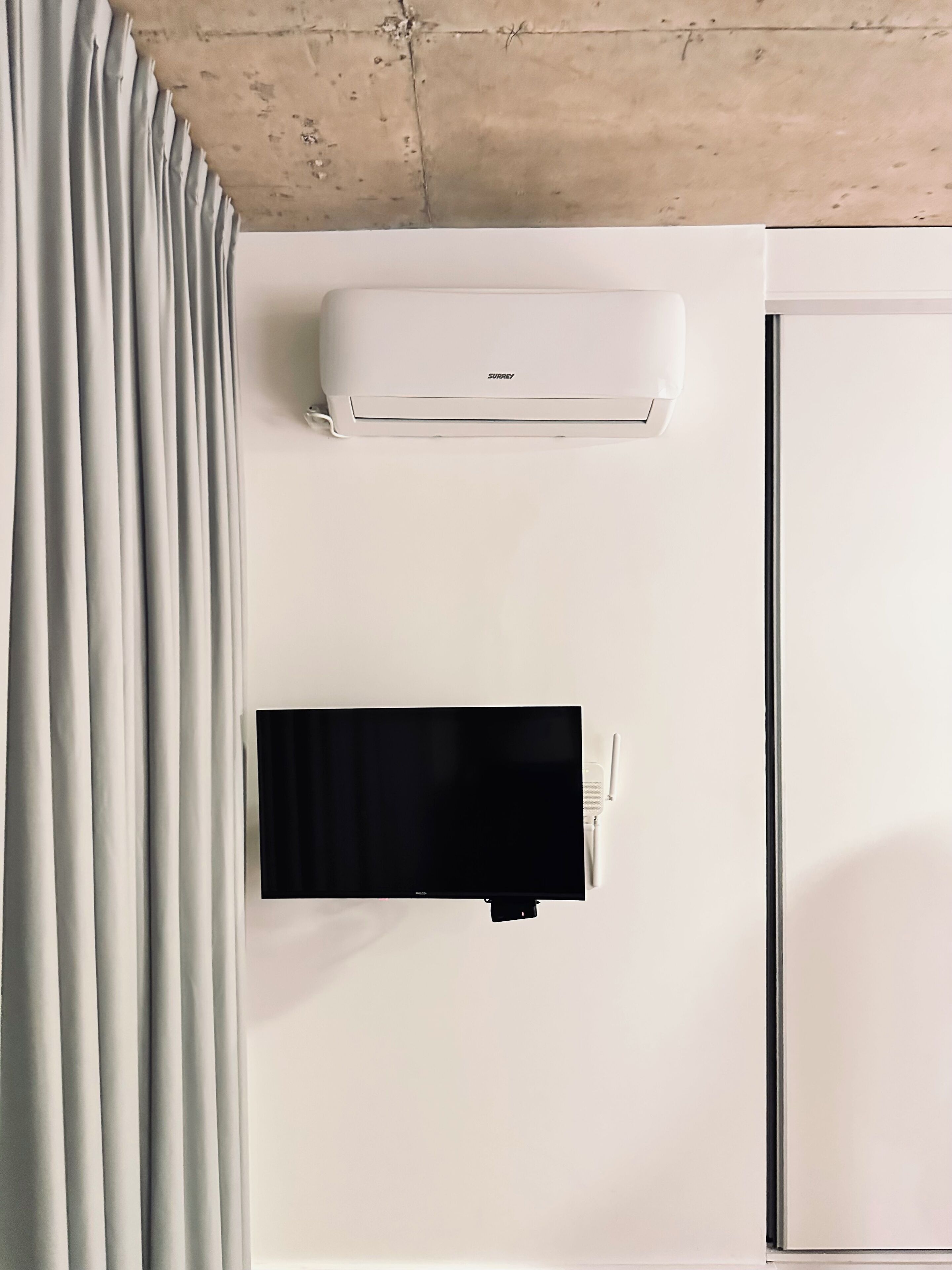A white wall with a mounted air conditioner and a flat-screen TV.