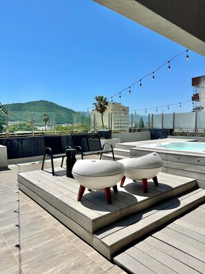 A rooftop terrace with two white cushioned seating areas, a hot tub, and string lights. - Just a few meters from Paseo Balcarce • Apartment with a View & Amenities   (Salta)