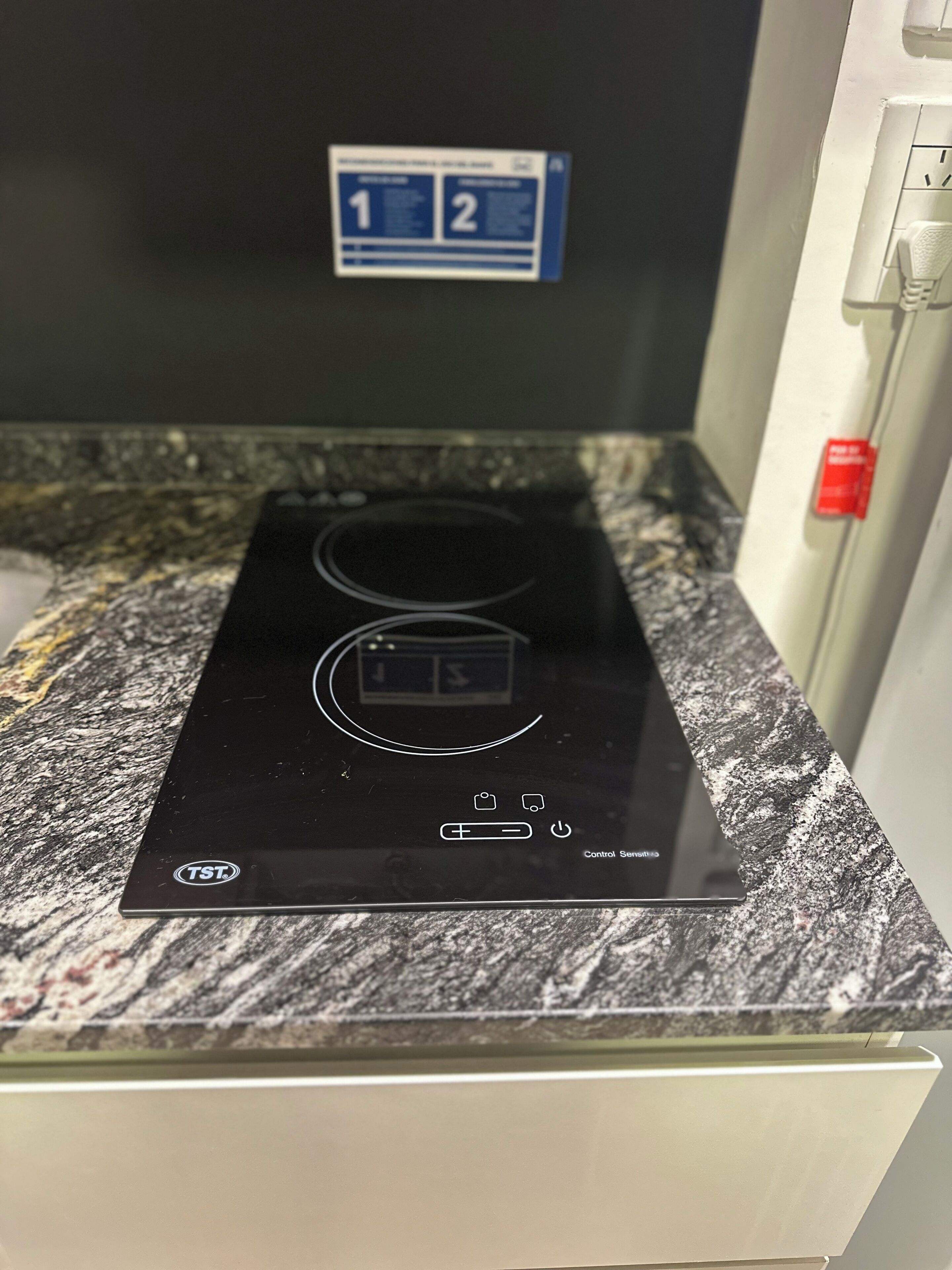 Een zwarte inductiekookplaat met een digitaal display en bedieningsknoppen op een granieten aanrecht.