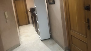 A corridor with a marble floor, wooden doors, and a white refrigerator. - Guest ROOM (Rabat)