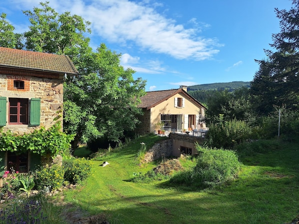A stone house with a garden, a small bridge, and a view of the forest.