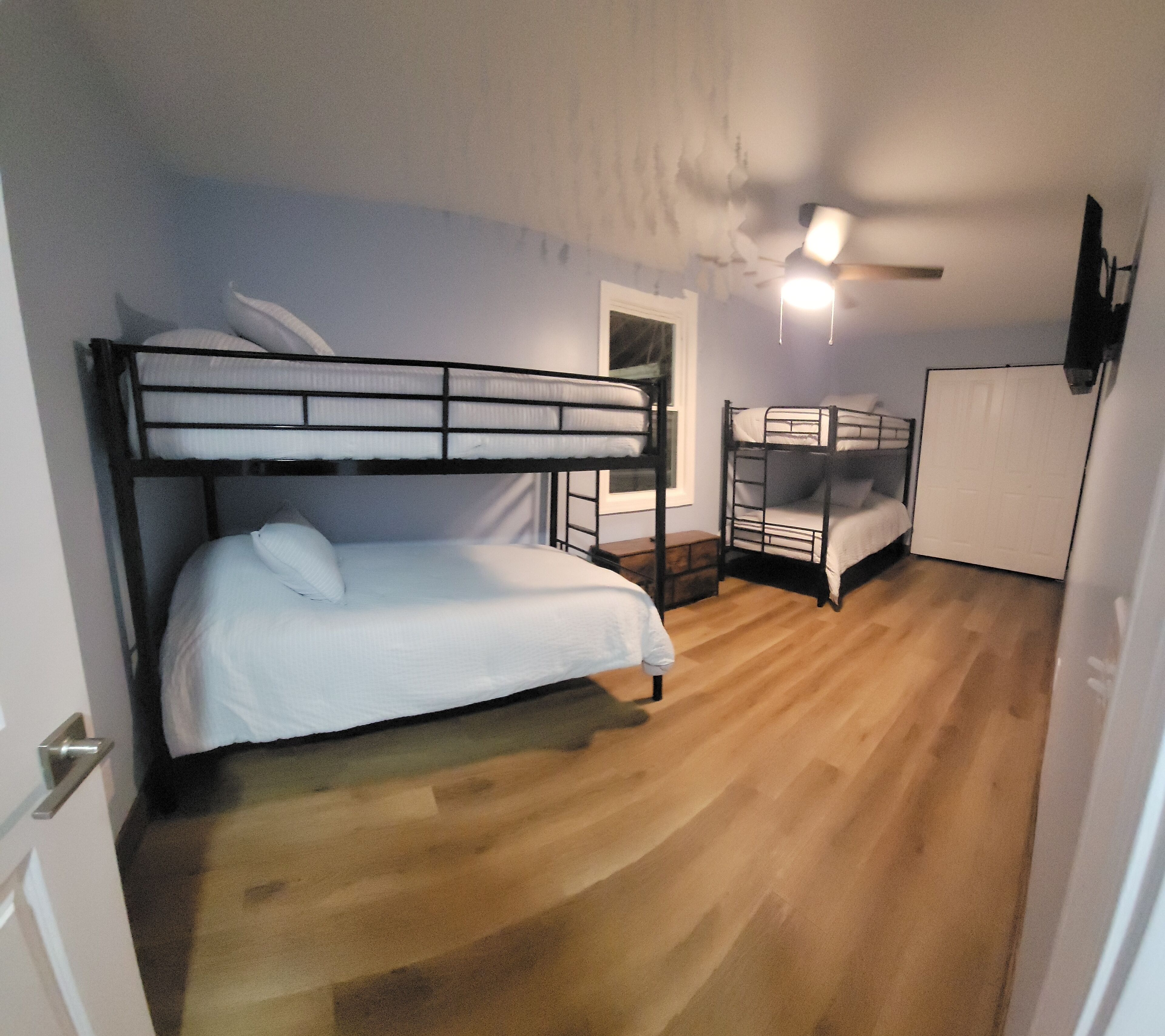 A compact room with bunk beds, a small wooden table, a white door, and a ceiling fan.